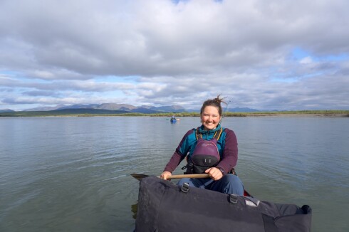 light-skinned woman wearing personal flotation device smiles as she holds paddle in canoe