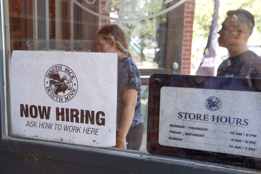 People walk by a "now hiring" sign.