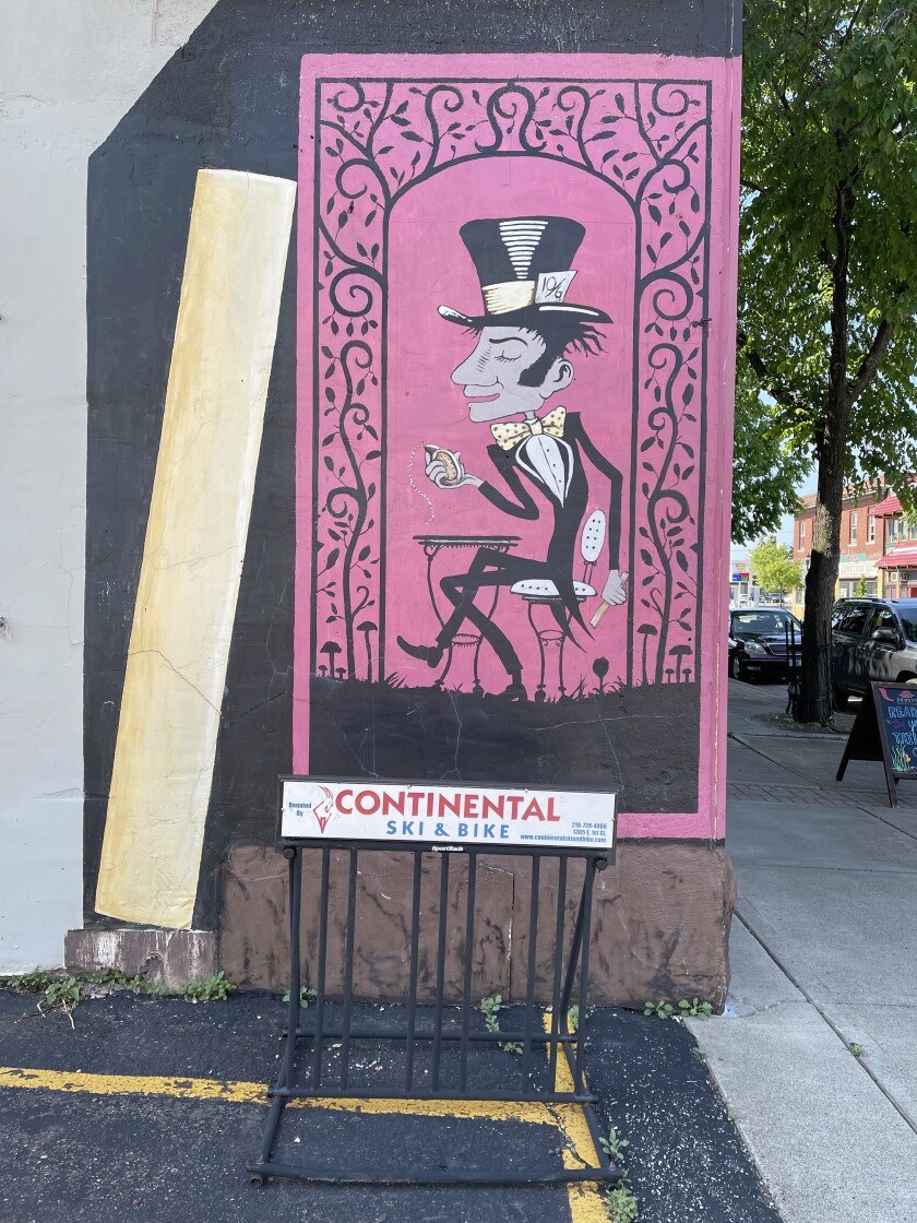 A bike rack marked CONTINENTAL SKI & BIKE stands near a pink-and-black mural depicting the Mad Hatter from "Alice in Wonderland."