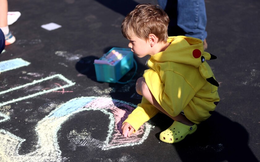 Boy uses chalk to color on a driveway