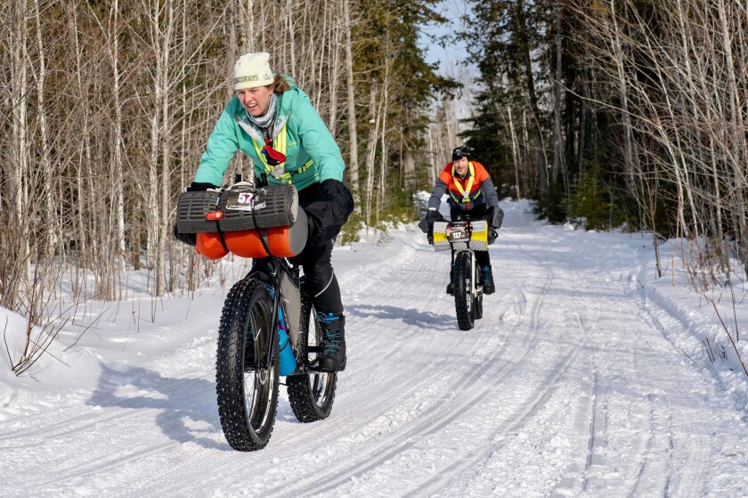 A man and women fat bike on a snowmobile trail.
