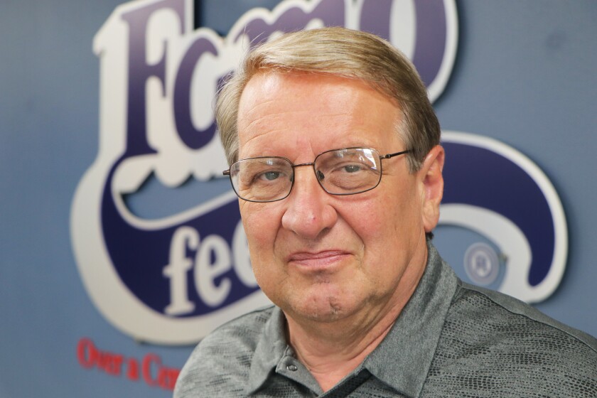 A graying man with eye glasses stands in front of a Famo Feeds Inc. wall logo.