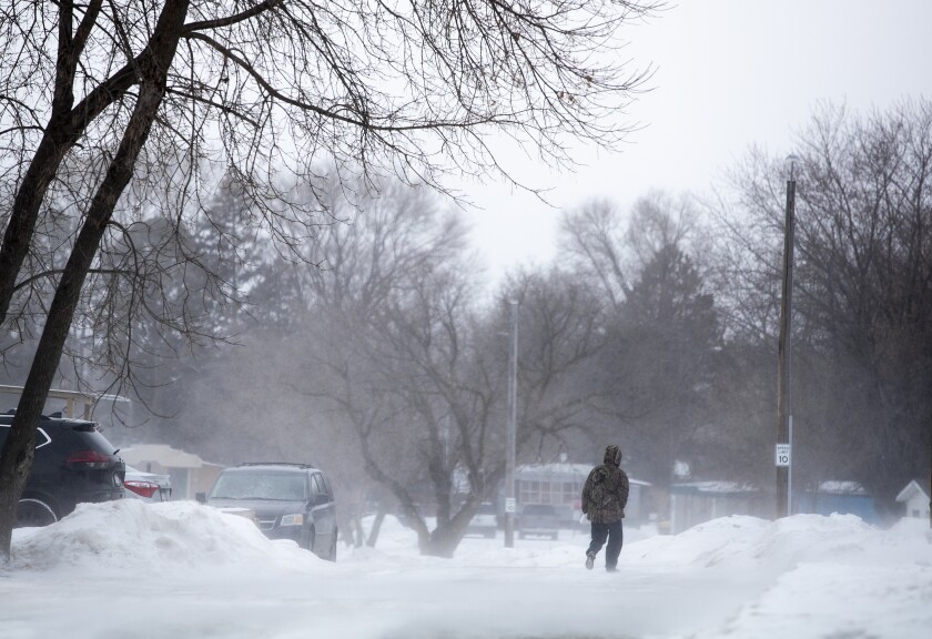 A man walks along South Mall Street as winds blow freshly-fallen snow around on the ground in Willmar Friday, Feb. 18, 2022.