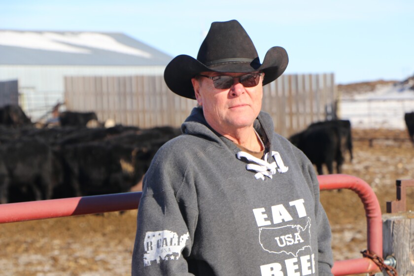 Rancher Ed Melroe of Kulm, North Dakota, poses in his cowboy hat in front of a cattle feedlot.
