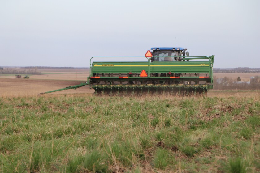 A no-till planter moves away, planting soybeans in one of last year's alfalfa fields as other farmers plant in the distance.