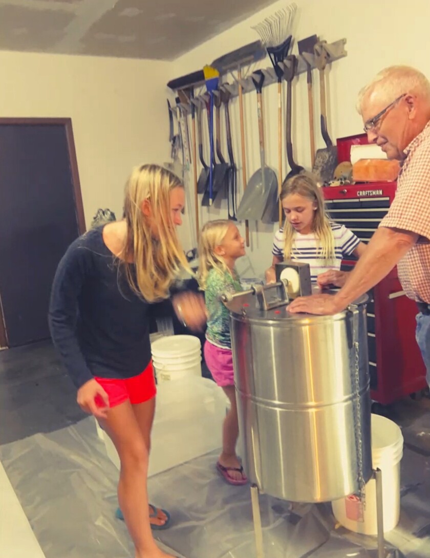 Meyer and her three granddaughters stand around a cylindrical honey extractor. 