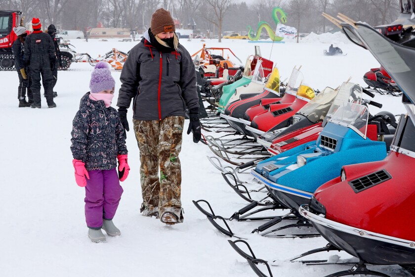 A mother and daughter look at classic snowmobiles on Serpent Lake in Crosby.