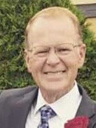 A man wearing glasses and a suit and tie smiles.