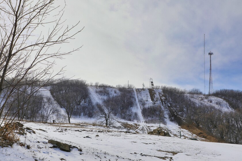 A wooded hill is seek in wintertime covered in a light layer of snow. Antennas are on top of the hill to the right of the photo.