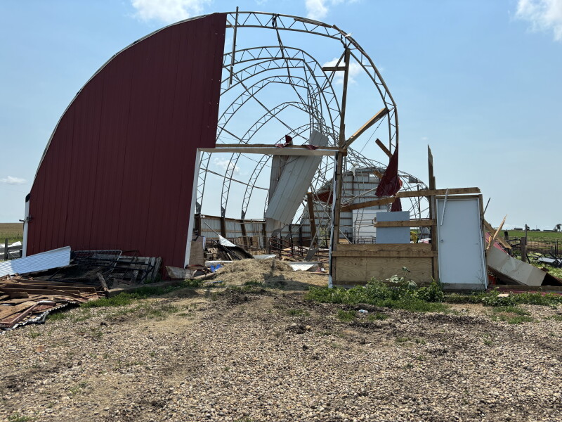 CDATA[
HIGHMORE, S.D. — Mel Leveque, the owner of AeroAg Drone Services and a rancher outside of Highmore, said a June 29, 2026, storm that hit Highmore and surrounding areas early in the morning came out of nowhere.
“I’ll say, 5:30 our phones started going off, and it said, you know, possible gusts of wind up to 100 mile an hour and, you know, we didn’t think much of it. We looked outside, and it was just really hazy, and the sun was coming up so it was orange. It was kind of wild,” he said.
The storm, which produced gusts as high as 131-miles-per-hour, caused heavy damage to crops, livestock and infrastructure in the area, and ag producers there say recovery will take time.
Marilyn Hanson and her daughters Elissa Schultz and Rachell Fletcher run the Dakota Wind Meat Goats and crop operation 8 miles southeast of Highmore. They raise corn and soybeans and have 500 head of meat goats. They have been farming there for 15 years. After getting the storm alerts, Fletcher, who lives in Highmore, secured things outside before heading to the basement.
“It sounded like and felt like a freight train hitting,” Fletcher said.
Fletcher said her brother, who lives at the farm site, quickly shut the doors of the barn because goats don’t do well in wet conditions.
“Goats really require having shelter when it rains. So they all ran into the barn, and I guess the wind was blowing so bad, it was raining so hard that you couldn’t even see your hand in front of your face,” Fletcher said.
Leveque said the rain started before the wind picked up.
“The wind hit and we couldn’t see a foot out of the windows. We all went in the basement and it started to hail,” Leveque said. “It was over pretty quickly. It just kind of hit really hard.”
The damage
David Karki, crop production extension agronomist for SDSU Extension, drove through the area after it was hit with the storm.
“We saw the damage to a lot of infrastructures,” he said.
Schultz was returning from work after the storm hit. She said finding a route home took time.
“The first road I took, there was a tree down, and then I took another road, and I was able to go and my heart was broken when I went down the road and I couldn’t see the top of our hoop barn. I could tell, I couldn’t see the white top of it. So it was extremely devastating,” Schultz said. “I called mom first and said, ‘You better brace yourself, because it’s pretty terrible out here.’ And that was before I saw my place. It’s a quarter of a mile up the road. It’s even worse up there.”
The family received significant damage to their farming operation, including the loss of the hoop barn, which was their main kidding barn built in 2020, a shop and three other barns.
![