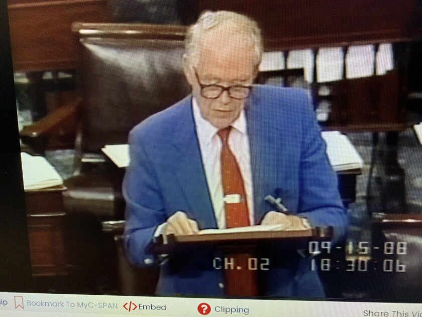 A man in a blue suit and red tie speaks on the Senate floor.