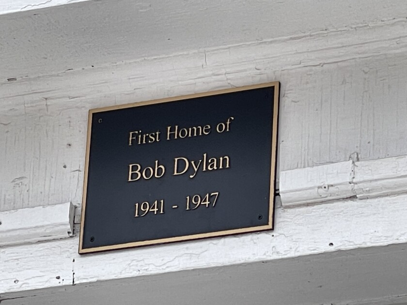 Metal plaque on wooden, white-painted external house beam reads "First Home of Bob Dylan 1941-1947"