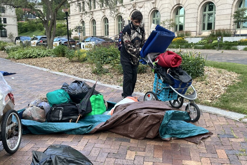 A man stands on the sidewalk among tarps, tents and other belongings