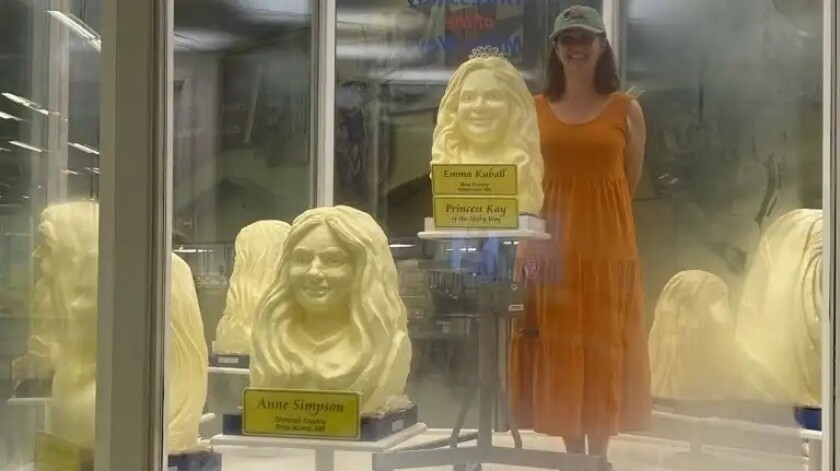 Žena v šatech a ballcap stojí vedle řady soch másla