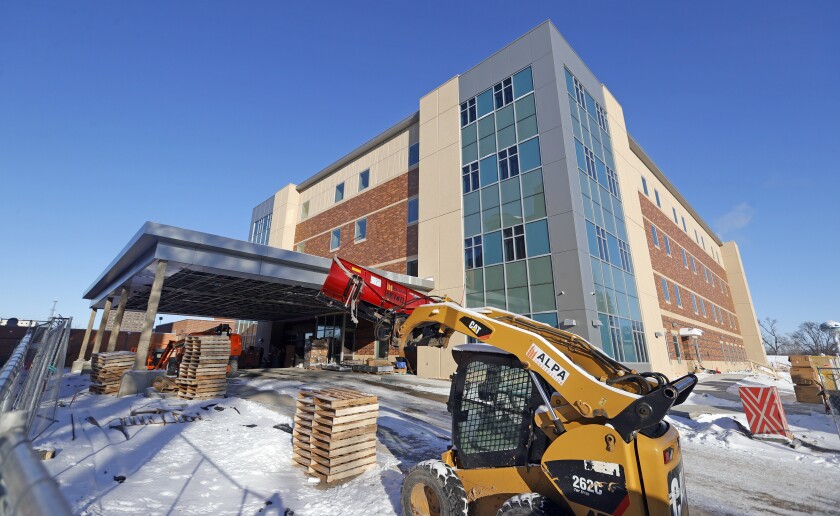 A backhoe and several stacks of pallets sit outside a new, rectangular building.