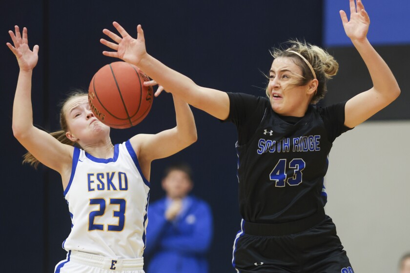Girls basketball players in black uniforms compete against players in white uniforms at a high school gymnasium.