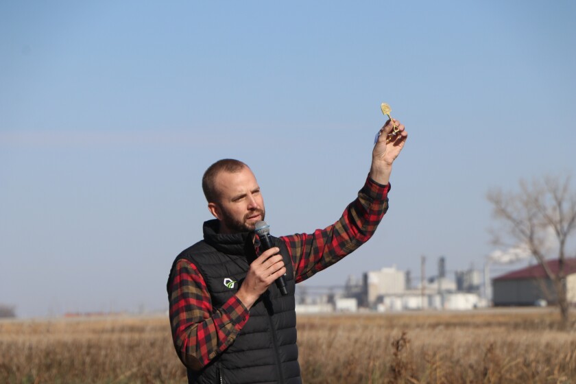 A man in a plaid shirt and vest holds up a tiny commemorative golden shovel, handed out at a groundbreaking.