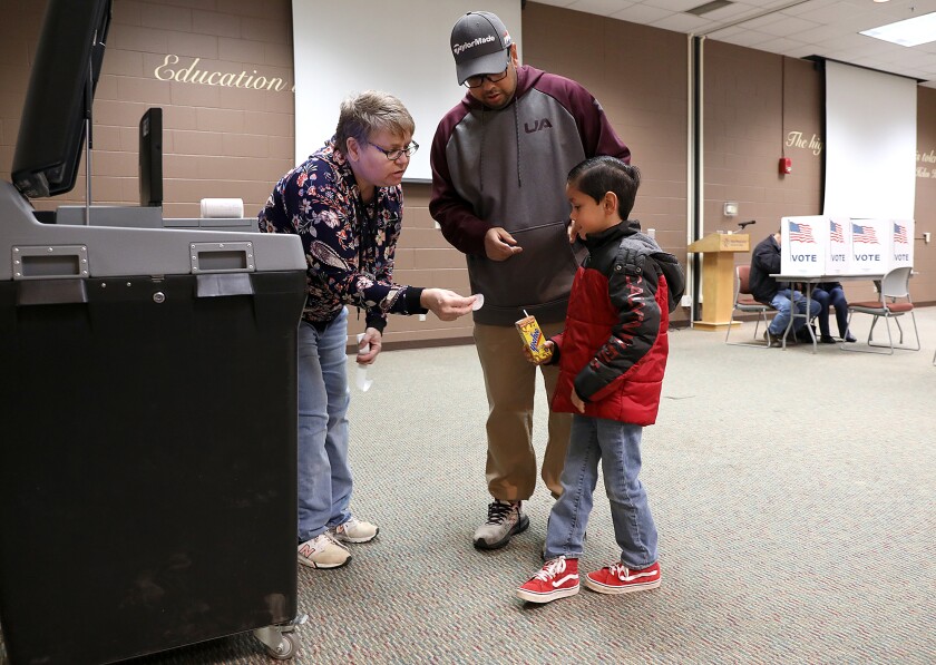 Election Inspector Carol Fransen, left, gives a sticker to Roman Durand, 6, after Michael Contreras cast his ballot at Northwood Technical College