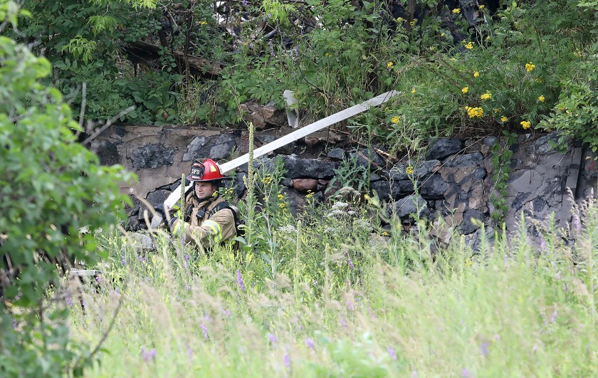 Duluth Fire Captain Rob Mesedahl pulls a hose through overgrown brush and down an old stone wall