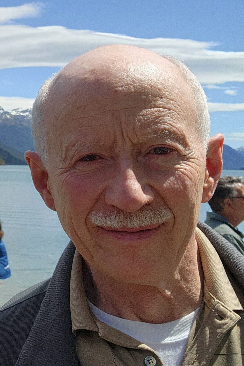 An elderly gentleman with short silvery hair and mustache smiles