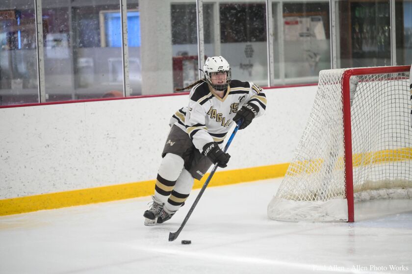 A hockey player wearing a white, beige, and brown jersey skates with the puck up the ice.