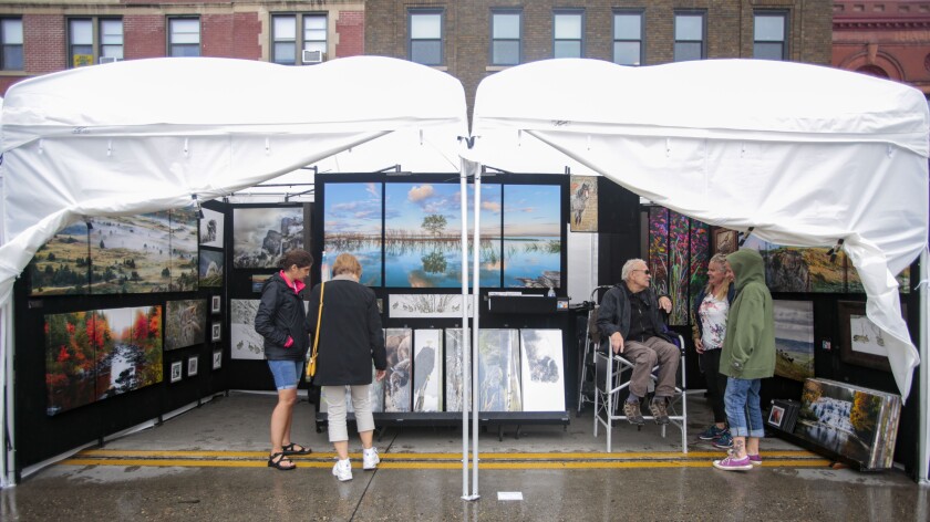 Photographer Pat Gerlach talks with his wife and daughter while visitors look at his work Thursday, July 19, 2018, in Gerlach's booth at the Downtown Fargo Street Fair. Erin Bormett / The Forum
