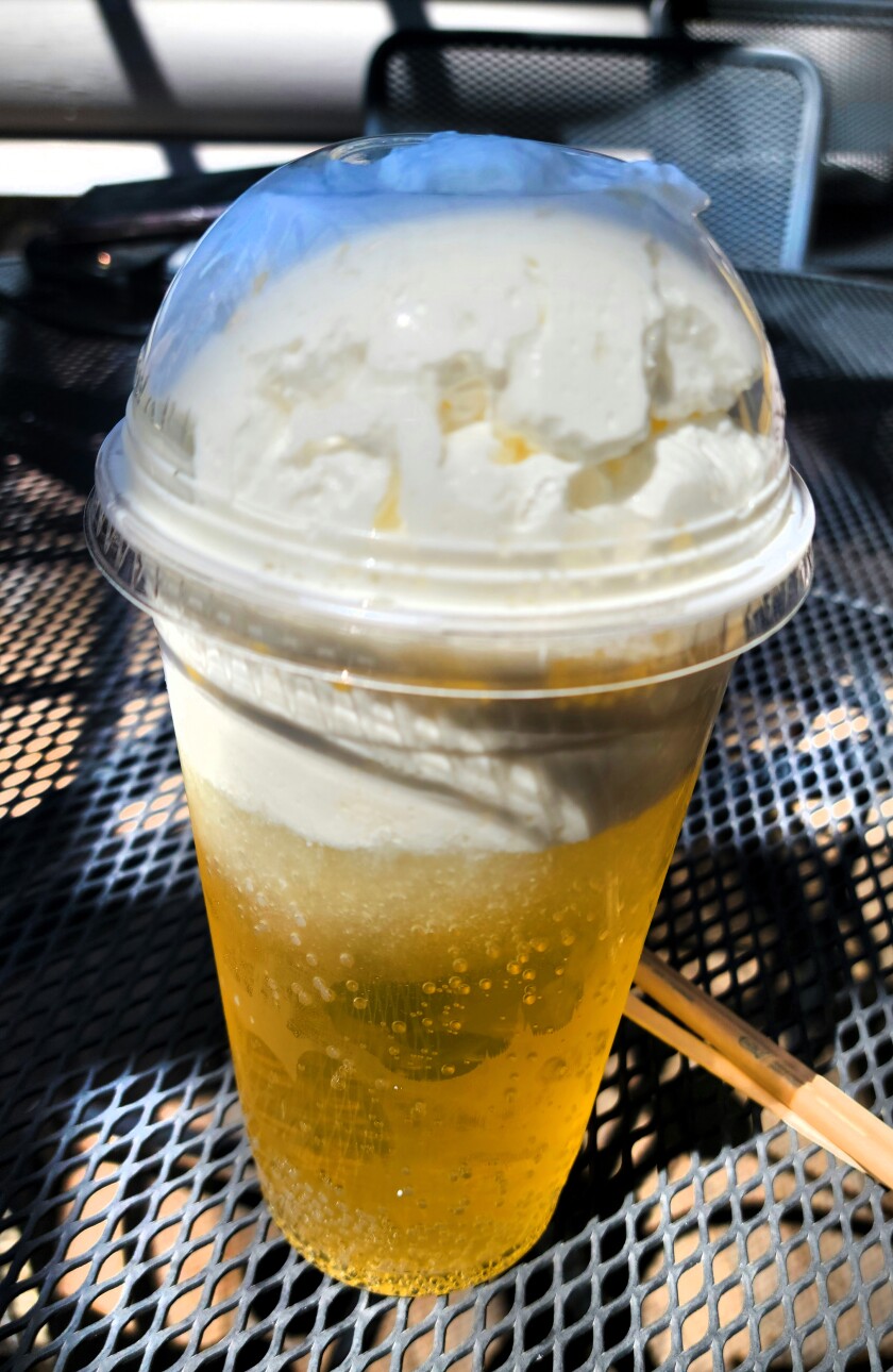 A yellow orange bubbly soda is topped with a heaping amount of white whipped cream.