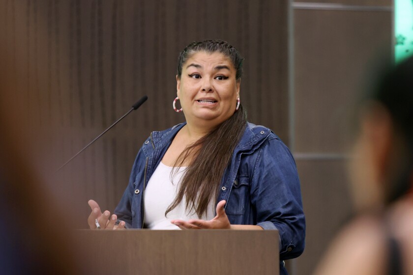 A woman with long hair gestures at a podium.