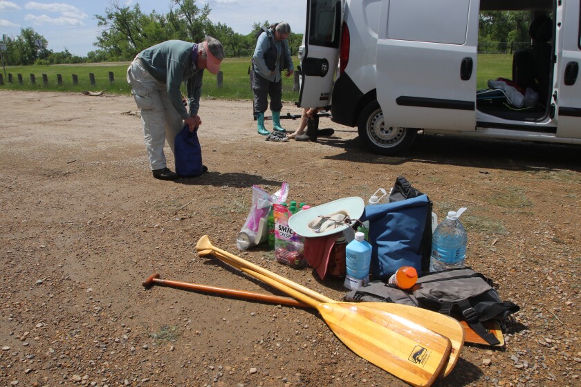 Paddles and bags of gear are stacked on the dirt.