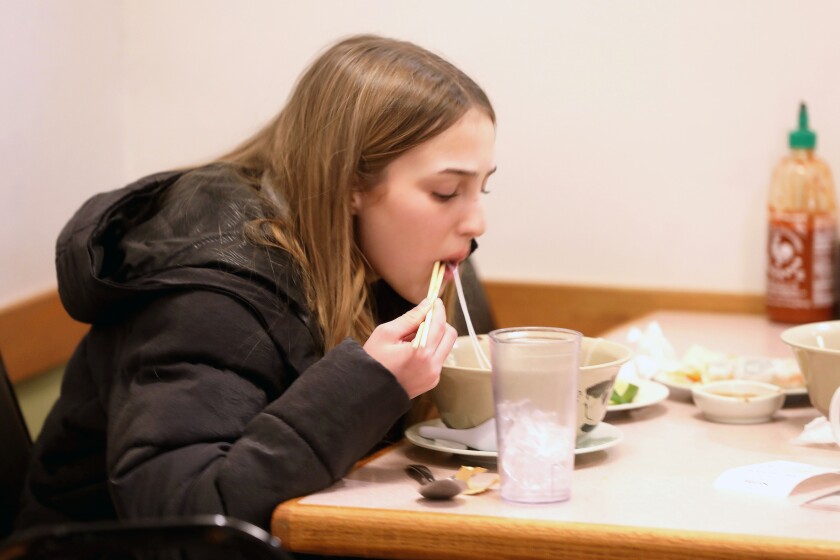 A young girl eating food with chopsticks at a restaurant.