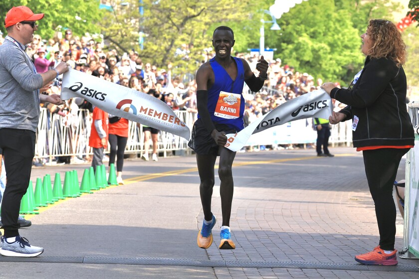 Dark-skinned man in blue top and black shorts crosses finish line