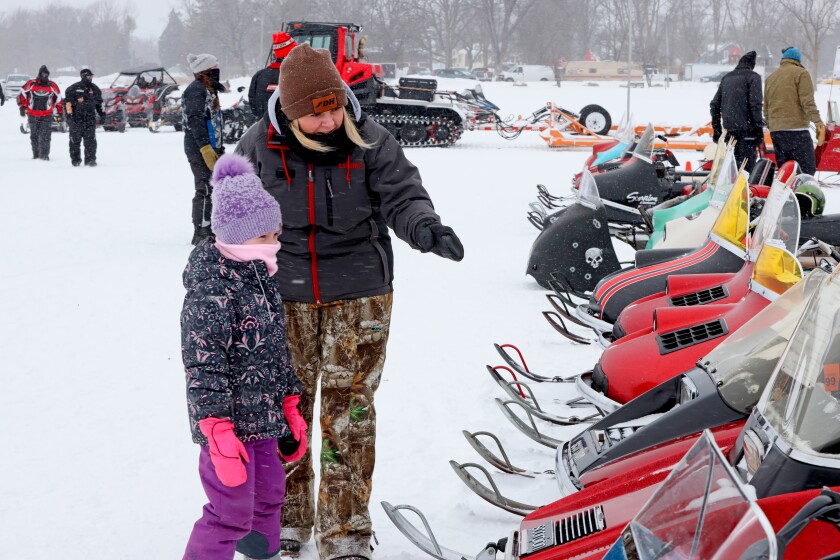 A mother and daughter look at classic snowmobiles on Serpent Lake in Crosby