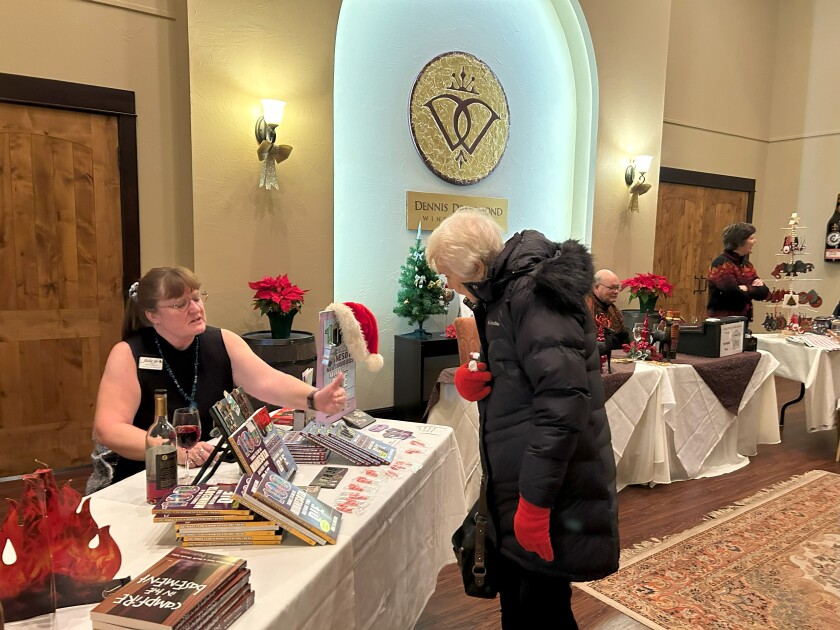 Author Julie Jo Larson sits at a table inside the lobby of Dennis Drummond Wine Co. in Brainerd on Tuesday, Dec. 19, 2023, to sign copies of her travel guidebooks.