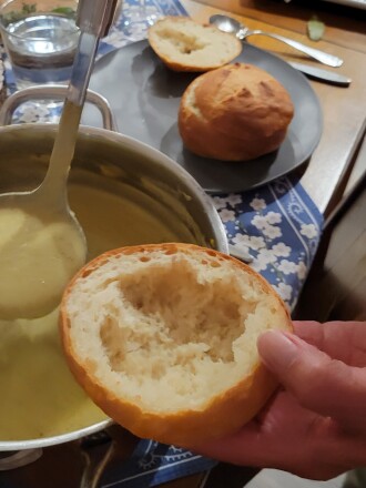 Ladling yellow soup from pot into bread bowl