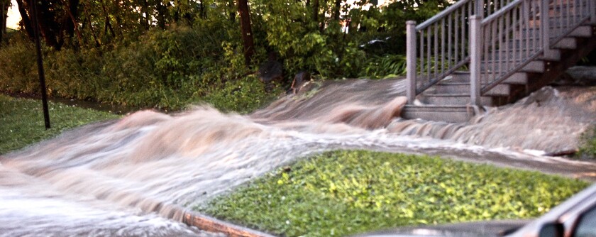 Rainwater pours down a sloped grass yard next to wooden stairs