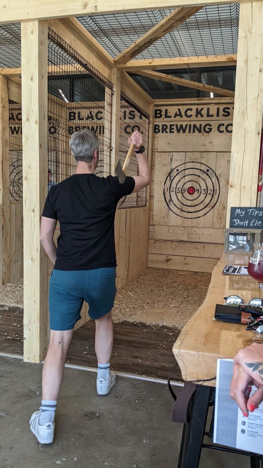 A man throws an ax at a wooden target labeled BLACKLIST BREWING CO
