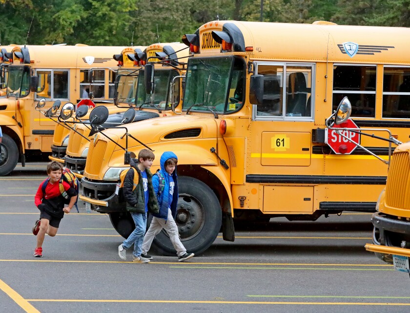 One kid runs past a couple of slower kids to get to the bus.