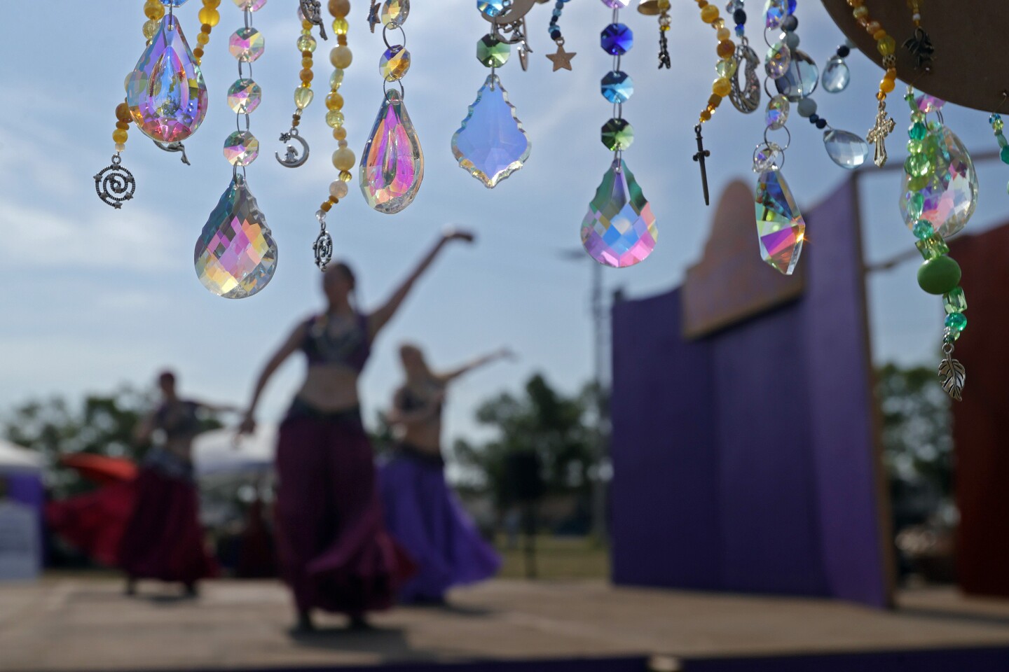 Crystals on chains in the foreground with artistic dancers in the background in a sunny setting.
