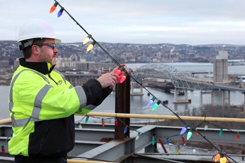 Man looks at lightbulbs high above bridge.