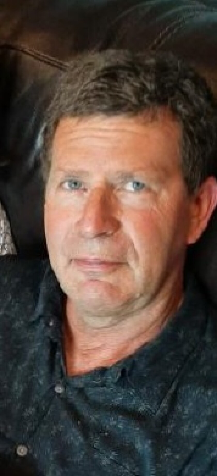 Caucasian Man in a dark button up shirt against a dark background.