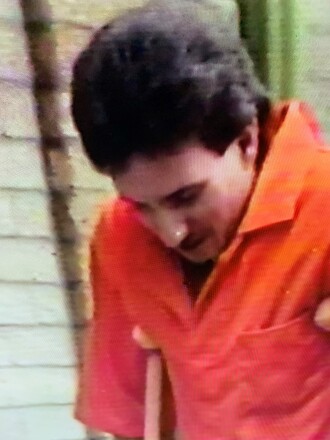 A man in an orange jumpsuit maneuvers with crutches.