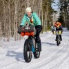 A man and women fat bike on a snowmobile trail.
