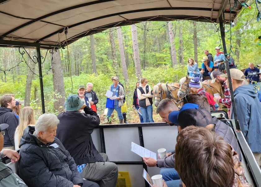 People gather in a wagon with others standing nearby and a horse-drawn cart for a Forestry Field Day.
