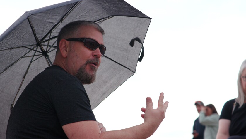 A man in sunglasses gestures and holds an umbrella.