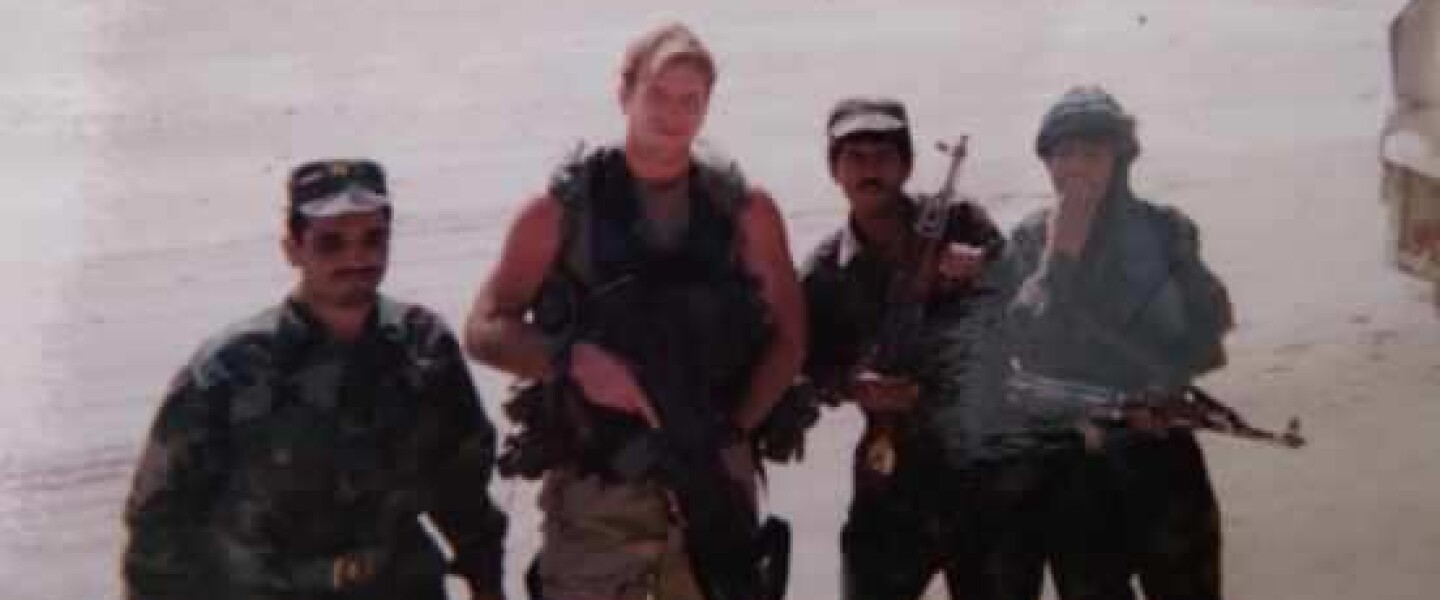 Four men pose with rifles.