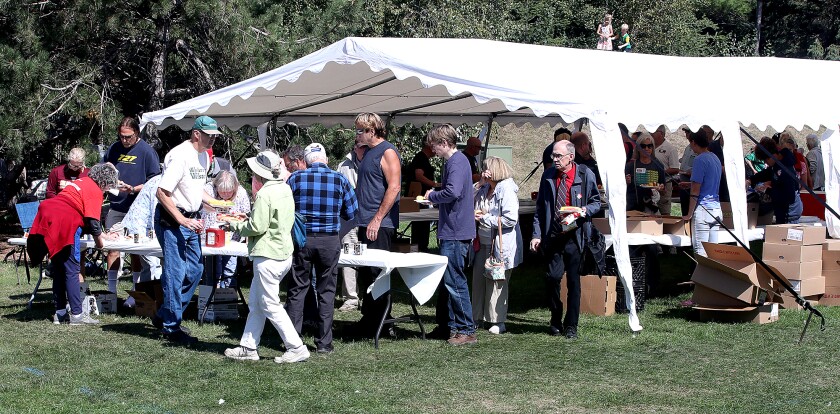 Folks add condiments to their hot dogs and corn after waiting in line for food
