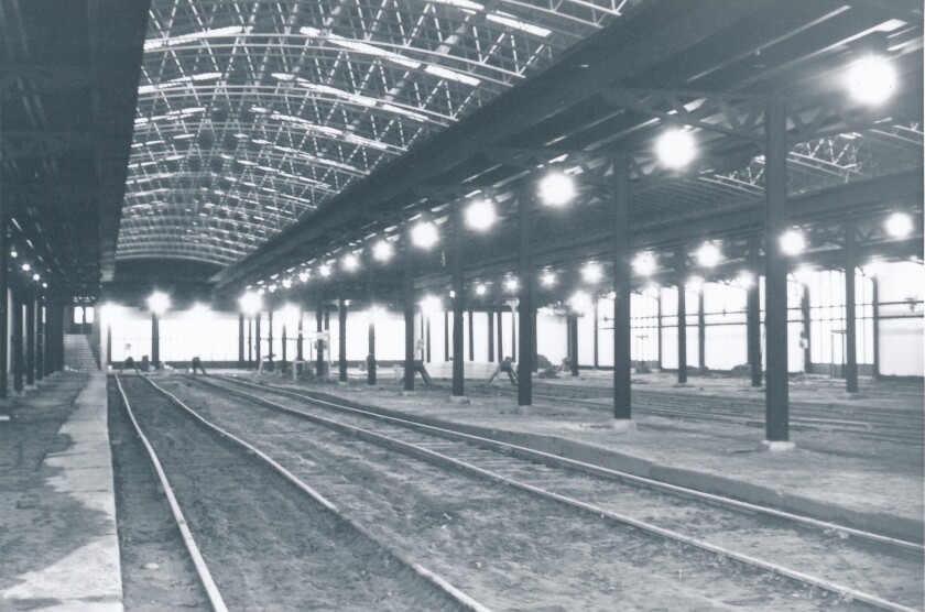 In a black-and-white image, an empty trainshed encloses several tracks. Vaulted skylight runs along center.