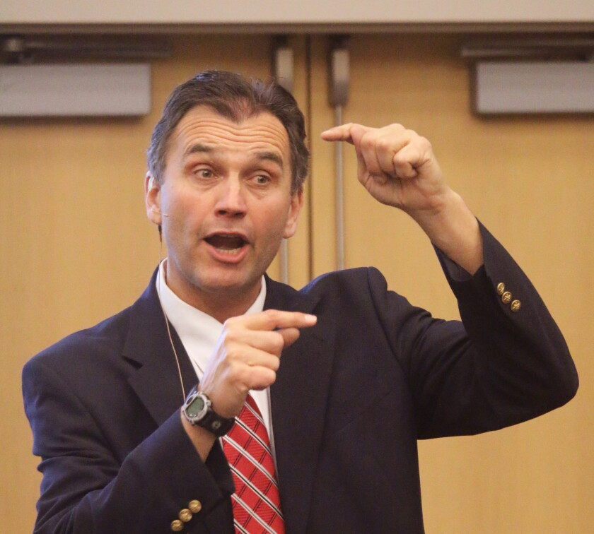 A speaker in a suit speaks to an audience, using his hands to show the impact of dicamba on non-tolerant soybeans.