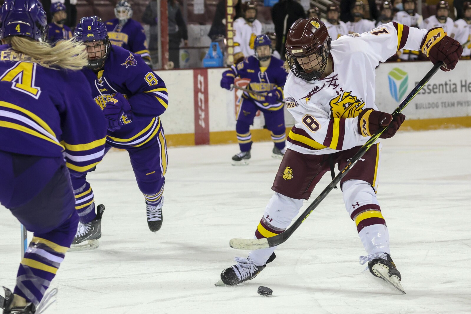 Women hockey players in purple and yellow compete against players in white and maroon at Amsoil Arena