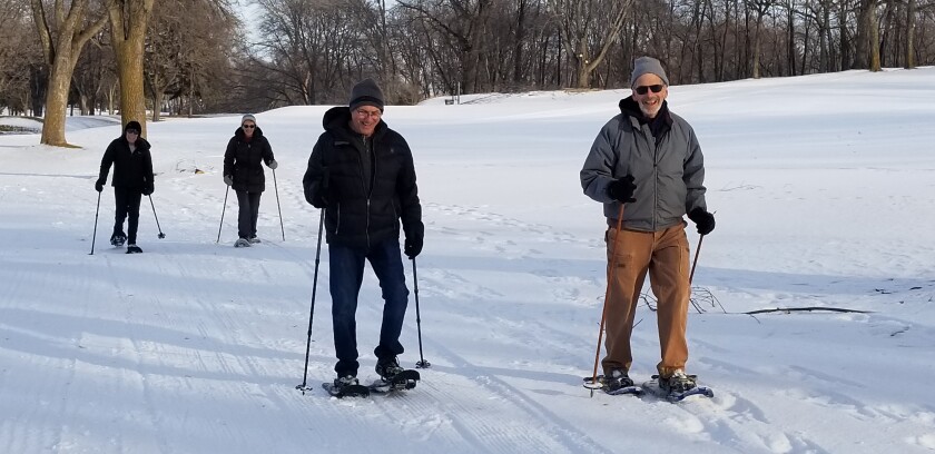 Four people are snowshoeing along a snowy trail.